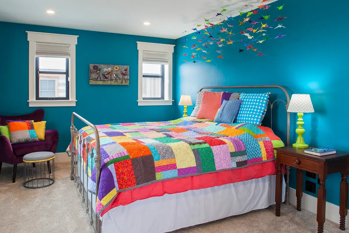 Colorful kids bedroom in a Crested Butte home with a patchwork quilt, vibrant blue walls, and origami crane mobile suspended from ceiling.