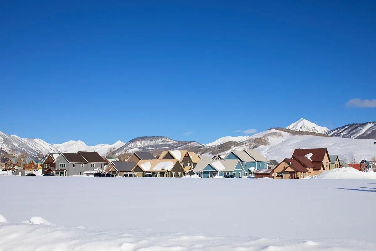 A snow-covered cluster of colorful duplex homes in Crested Butte set against bright blue skies and mountain peaks.