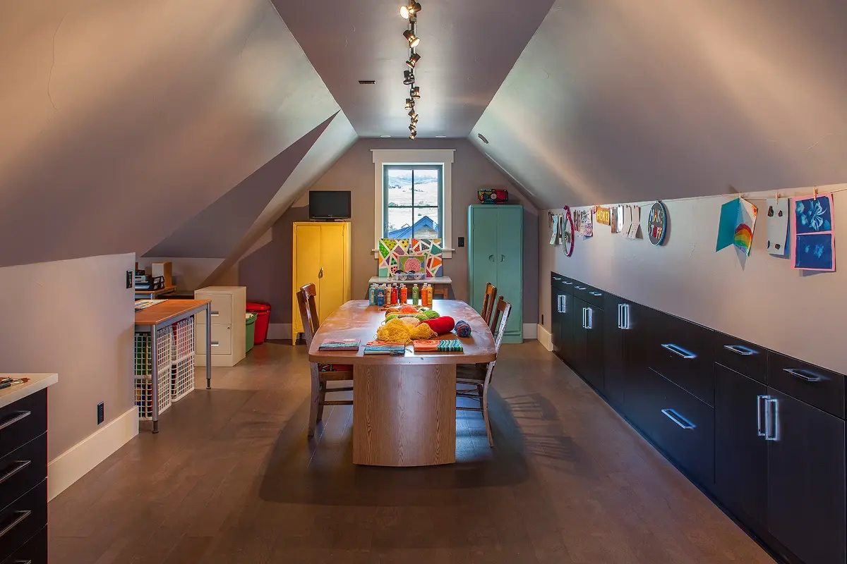 Third-floor attic craft room designed by Crested Butte architects with sloped ceilings, black cabinetry, and a central workspace.