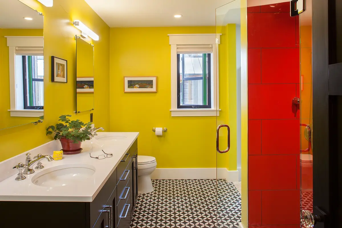 Bold yellow bathroom with black cabinetry, geometric floor tiles, and a vibrant red tile shower in a modern Crested Butte mountain home.