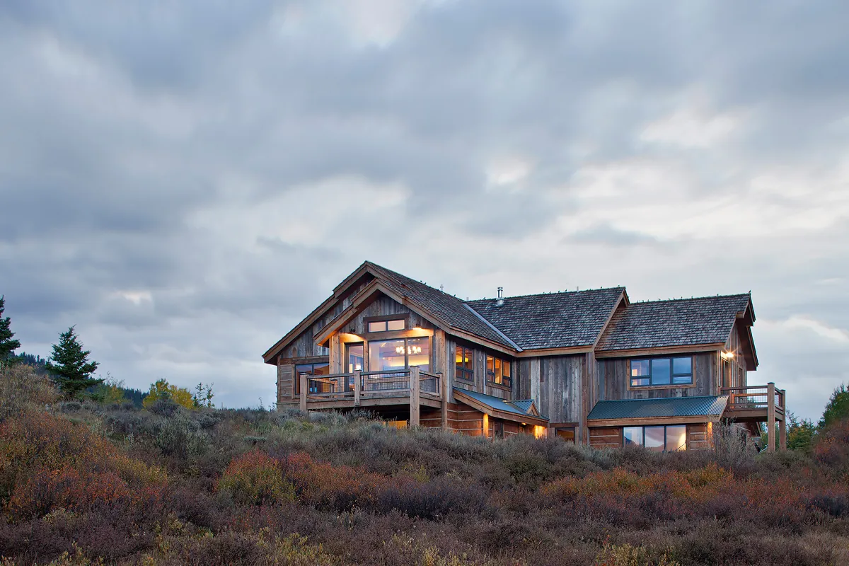 Evening view of modern rustic mountain home with wood siding and steel rooflines nestled in Colorado brush.